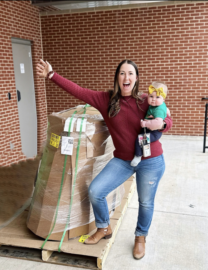 Teacher Standing on large box of delivered couch holding a baby